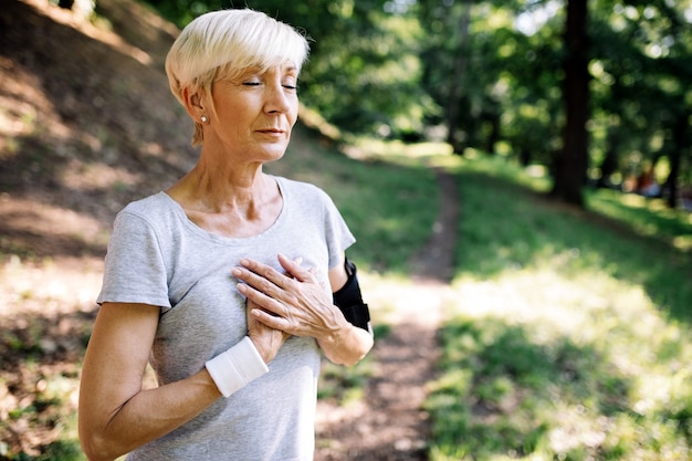 Senior woman with chest pain suffering from heart attack during jogging