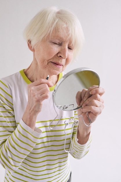 senior woman with eyebrow tweezers and small mirror plucking her beard