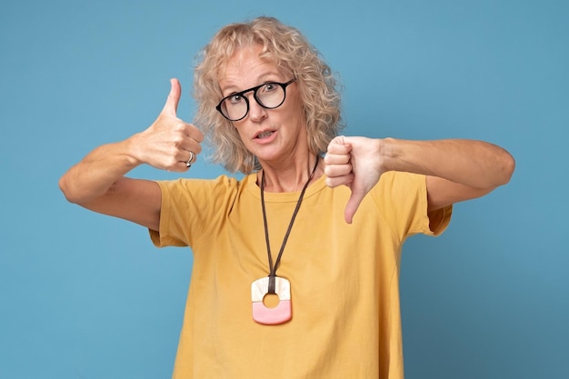 Senior woman with glasses showing thumbs up and thumbs down\
difficult choose