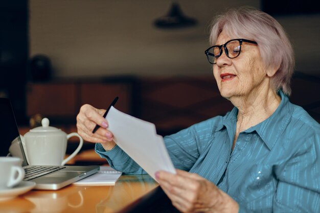 안경을 쓴 고위 여성이 노트북 앞 테이블에 앉아 있다