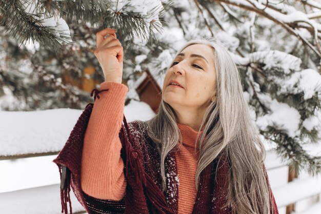 Photo senior woman with gray hair in a knitted sweater and scarf sincerely smiling on a winter background