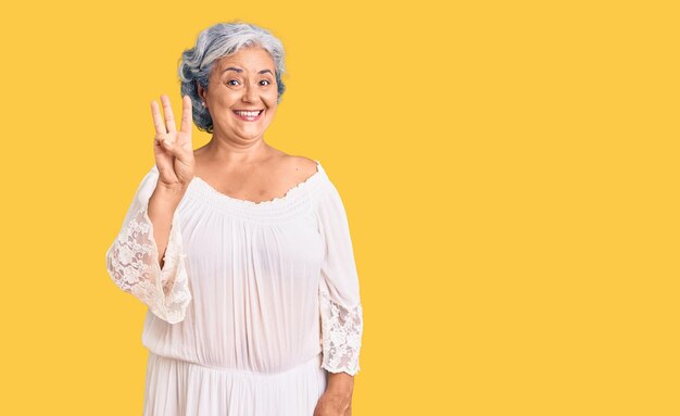 Senior woman with gray hair wearing bohemian style showing and pointing up with fingers number three while smiling confident and happy.