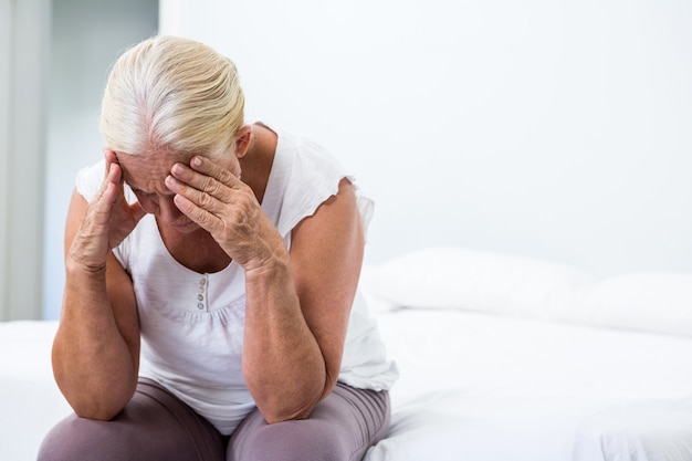 Donna senior con la testa a disposizione che si siede alla camera da letto