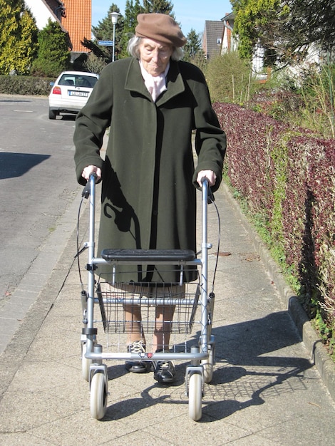 Foto donna anziana con un passeggino per la mobilità su strada