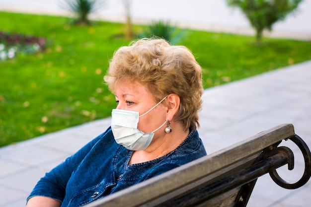 Senior woman with protection medical mask in park on bench  Elderly at risk for coronavirus covid-19