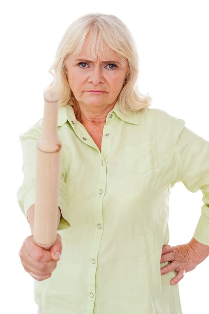 Photo senior woman with rolling pin. angry senior woman holding rolling pin and looking at camera while standing isolated on white background