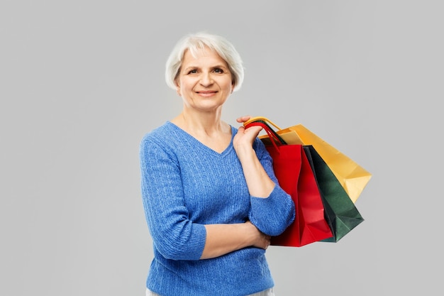 senior woman with shopping bags over grey