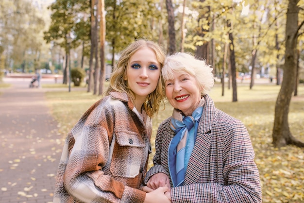 senior woman with young daughter walking outdoor in autumn park Family generation care love