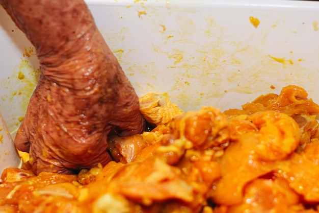 senior womans hand repairing a plate with raw chicken in the kitchen