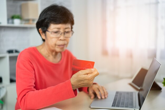 Senior women looking for credit card and using laptop shopping online