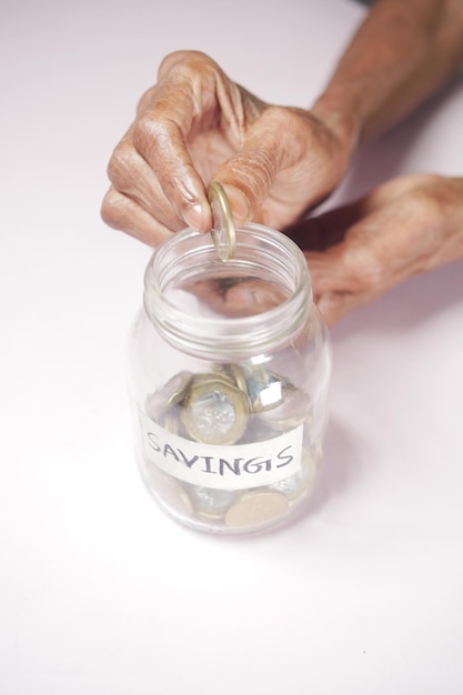 Photo senior women saving coins in a jar white sited