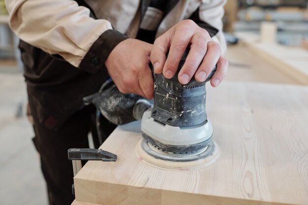 Senior worker of modern factory using touchpad while explaining his young colleague how to process wooden workpiece with grinder