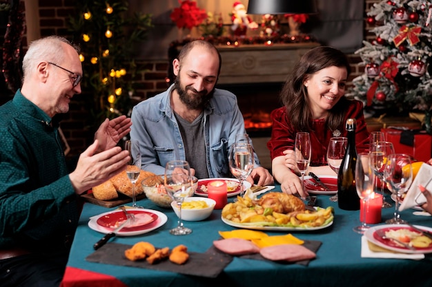 クリスマスイブに年長者と若者がテーブルに集まり、手作りの食べ物を食べたり、ワインを飲んだりして、一緒にお祝いします。多様な家族や友人が 12 月の休日を楽しんでいます。