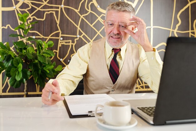 Senior zakenman bril aan te passen en zakelijk contract lezen wanneer u aan café tafel zit