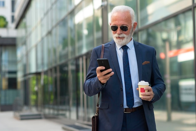 Senior zakenman die telefoon gebruikt om buiten een bericht te verzenden