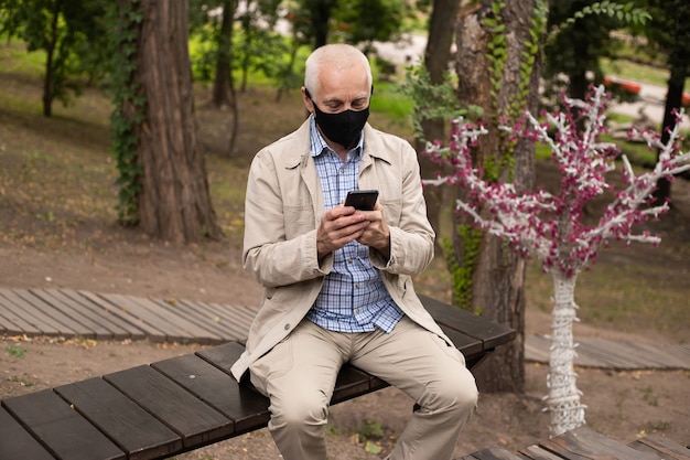 Senior zakenman dragen masker met smartphone in park