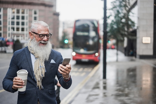 Senior zakenman gaat werken en drinkt koffie met het busstation van londen op de achtergrond - focus on face