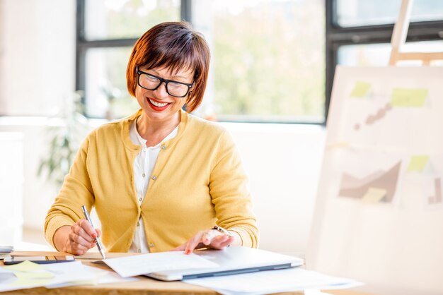 Senior zakenvrouw die werkt met documenten in het lichte moderne kantoorinterieur