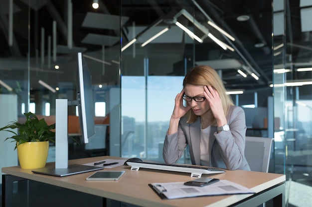 Senior zakenvrouw heeft ernstige hoofdpijn tijdens het werken in een modern kantoor op de computer