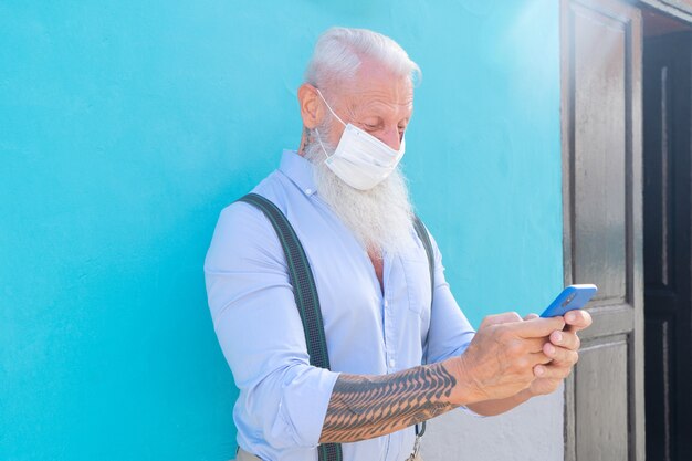 Senior zelfverzekerde man plaatsen op masker tegen blauwe muur tijdens uitbraak van coronavirus