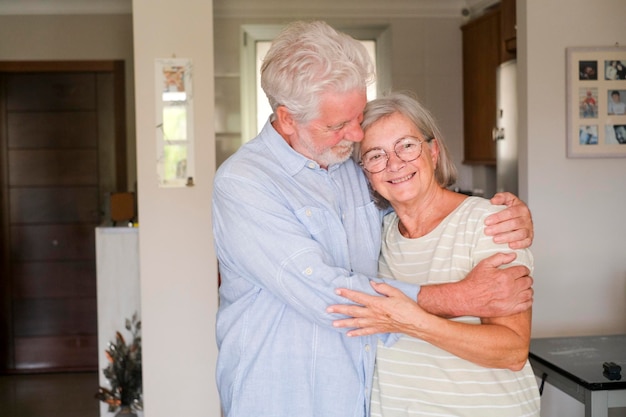 Senioren koppel knuffelen en glimlachen met appartement op de achtergrond Concept van het leven samen voor altijd ouderen Volwassen man en vrouw genieten van binnen recreatieve activiteiten met een portret in de woonkamer huis