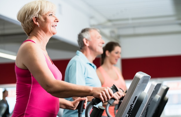 Senioren trainen op crosstrainer met personal trainer aan de g