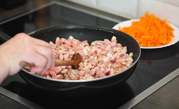 高齢者の女性の手は木のスプーンを持ち、鍋で揚げながら肉をかき混ぜる