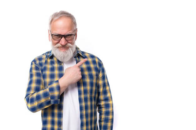 Senor grayhaired retired man with a mustache and beard points his finger to the side on a white