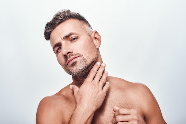 Sensitive skin handsome and sexy man touching his stubble and looking at camera while standing