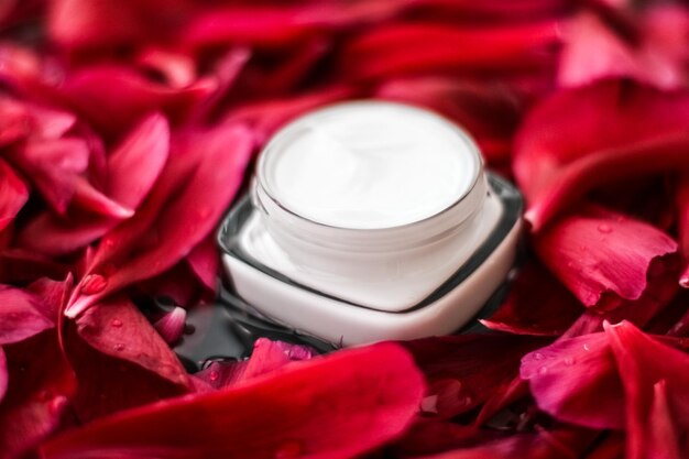 Sensitive skincare moisturizer cream on red flower petals and water background natural science for skin