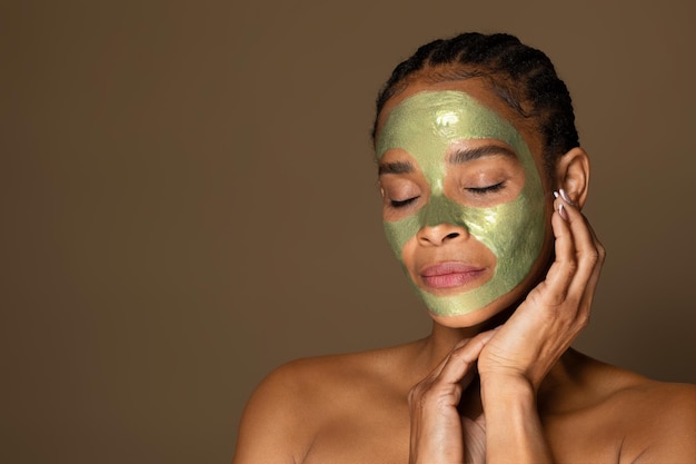 Sensual african american middle aged woman with green peeloff mask on her face posing on brown