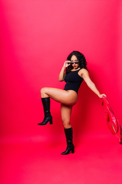 Sensual beautiful african ethnic woman in bodysuit posing in studio isolated on red white background