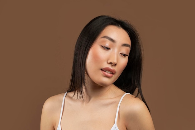 Photo sensual beautiful korean woman posing on brown studio background looking away enjoying her natural beauty