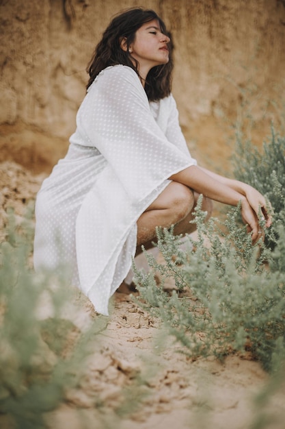 Sensual boho girl in white summer dress sitting on beach among
green bushes beautiful aesthetic image young woman relaxing on
seashore summer vacation tranquility