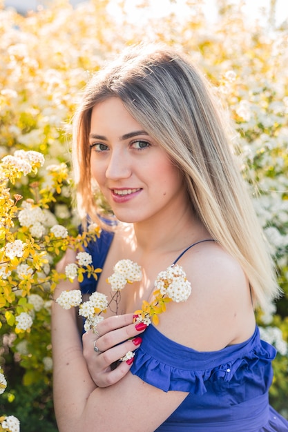 Sensual calm portrait of beautiful hipster woman in blooming bush with white flowers of spirea. Copy space. Stylish blonde woman in blue dress in garden