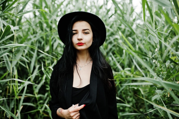 Sensual girl all in black red lips and hat Goth dramatic woman on common reed