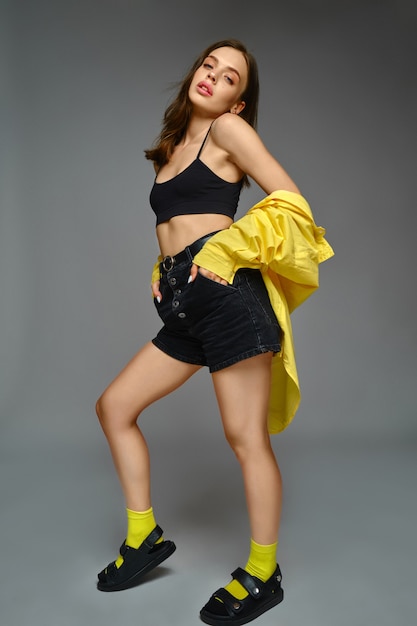 Sensual girl in black shorts top and yellow shirt against grey background