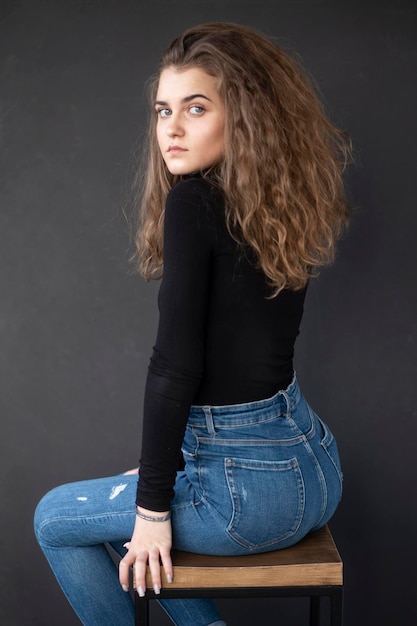 Photo sensual girl with curly hair sitting on high chair on a grey background