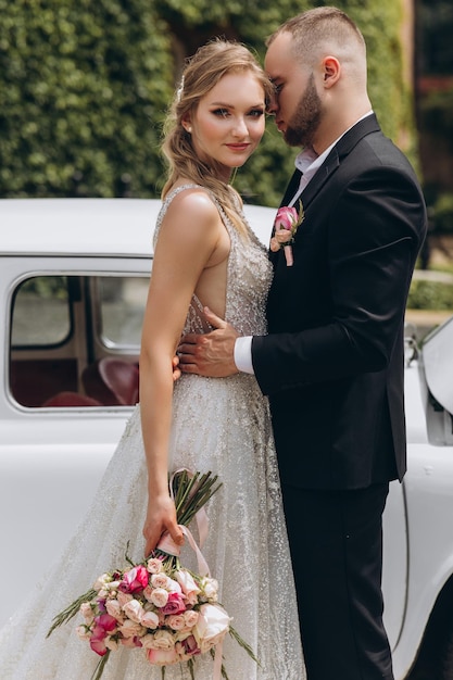 Sensual kiss of the two in their wedding day near retro car with flowers