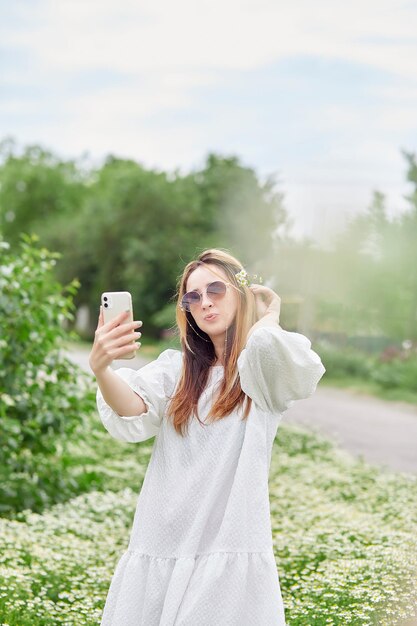 Sensuale donna millenaria che fa selfie nel campo della camomilla utilizzando la tecnologia blogging stile di vita rilassante e tempo libero