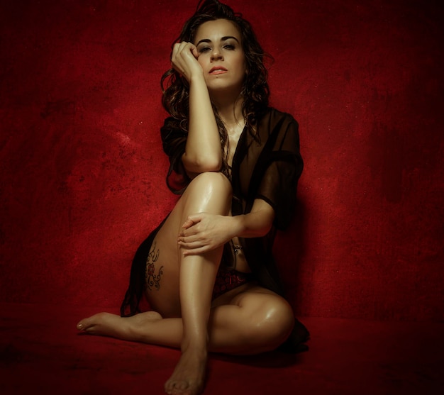 Sensual nude brunette woman with long black hair, on red wall with textures