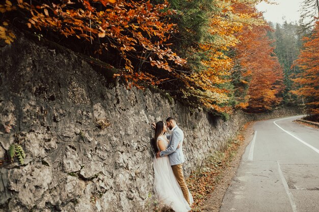 Foto sensuale di sposi sulla strada in montagna con alberi d'autunno.