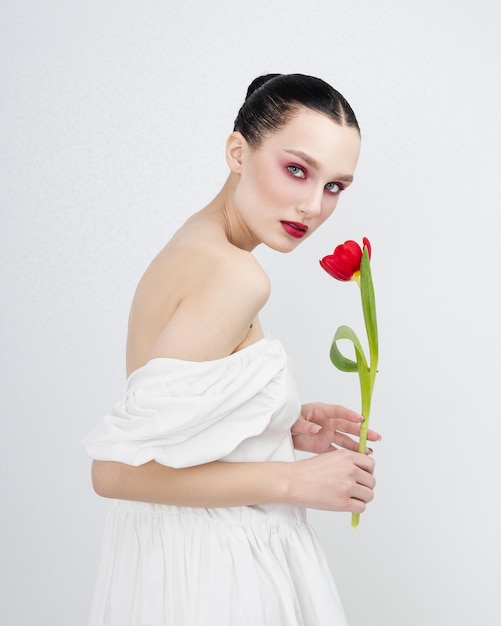 Photo sensual portrait of young attractive brenette woman holds of red tulips minimalist light pure photo shoot tenderness romantic international women's day