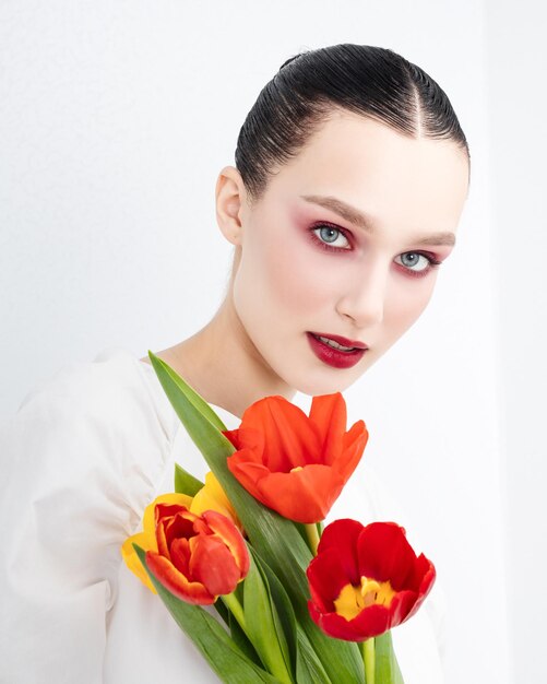 Photo sensual portrait of young attractive brenette woman holds of red tulips minimalist light pure photo shoot tenderness romantic international women's day