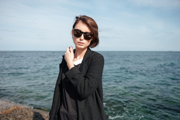 Sensual relaxed young woman in sunglasses standing near the sea