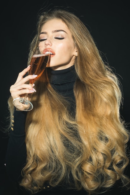 Sensual romantic blonde model in black clothes with long healthy hair enjoying champagne. Passionate sexy woman with gorgeous long hair, perfect makeup, sexy sensual lips, closed eyes drinks champagne