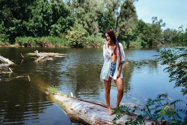 Sensual sexy brunette girl in an unbuttoned white shirt to undress near the river.