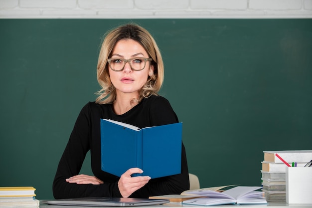 Sensual student woman in eyeglasses near blackboard Sexy girl sit on table on chalkboard Attractive female teacher in college Study concept