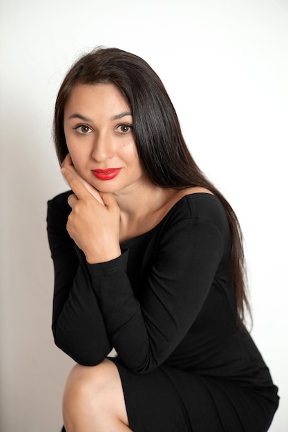 A sensual studio portrait of a beautiful young woman in a black dress with red lipstick on her lips White background place for text