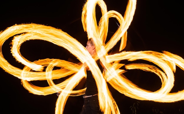 Sensual woman artist perform fiery twirly trails by spinning flaming pois during fire performance in night darkness outdoors pattern